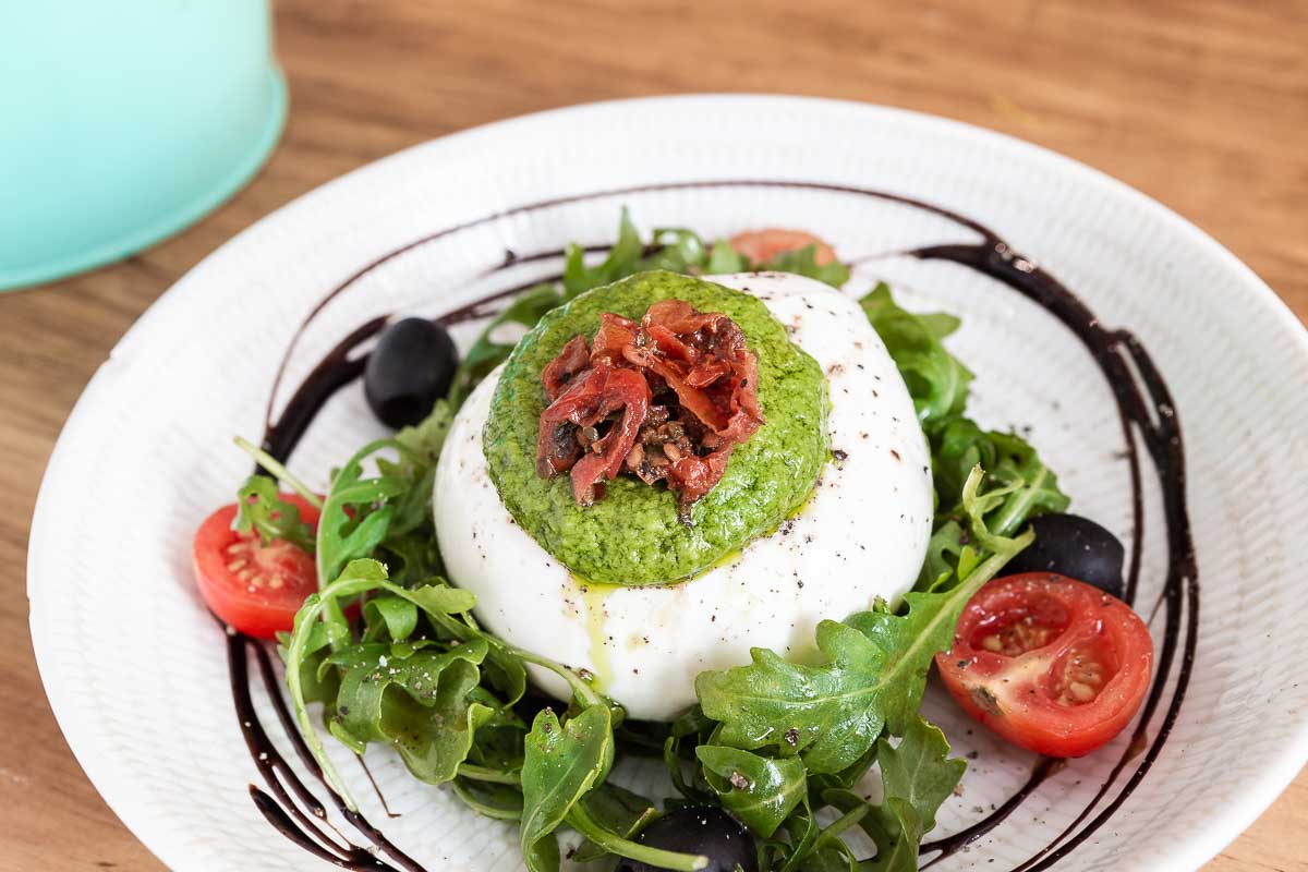 Burrata fresca con rúcula, tomate cherry, pesto de albahaca y frutos secos