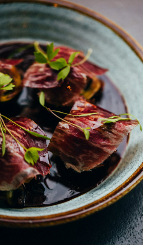 Alcachofas a la brasa con cecina de wagyu sobre un caldo de jamón y apionabo tostado