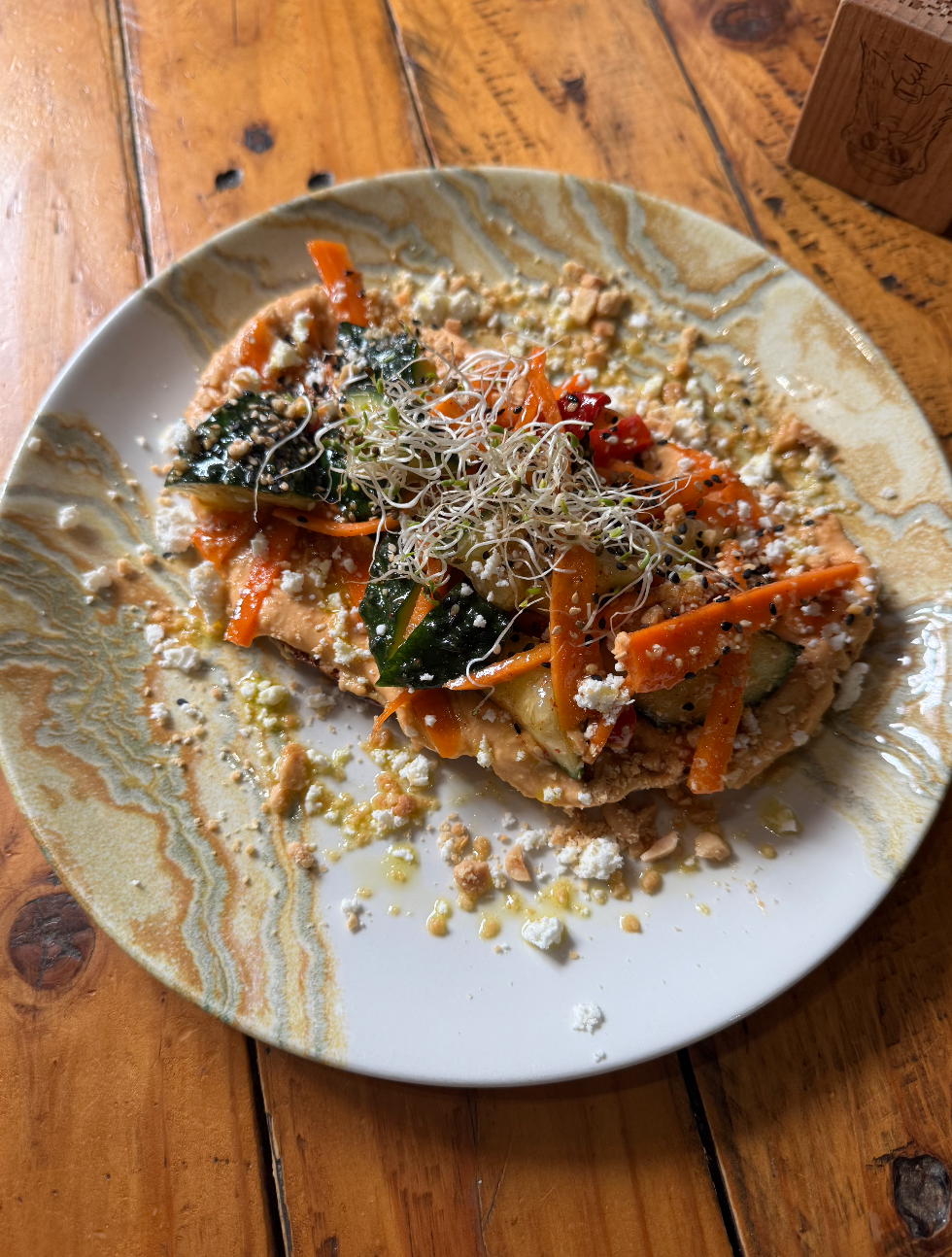 KIMCHI CHI . Tostada vegetariana: hummus de pimiento de piquillo, pepino y zanahoria encurtidos en kimchi, queso feta, cacahuetes y semillas de sésamo.