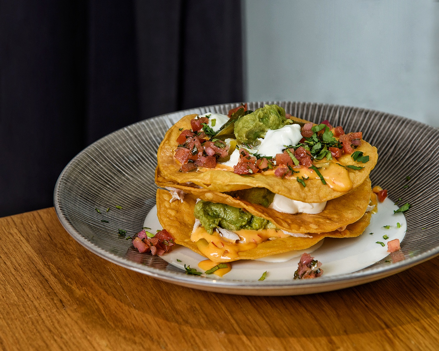 Crujiente de nachos a nuestro estilo con salsa de queso, pollo, pico de gallo y crema agria
