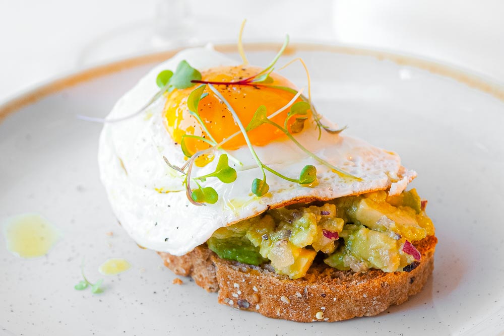Homemade avocado tartar on toast, grilled egg and fresh chives (vegetarian)